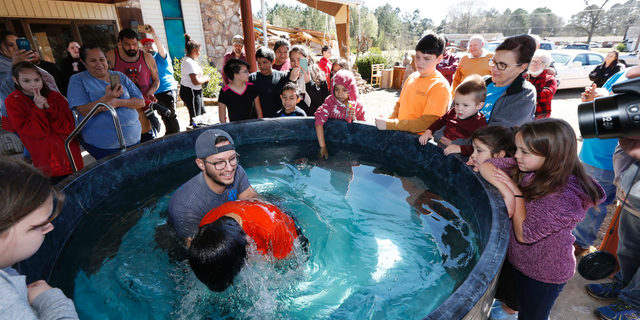 Church members watch as student pastor Craig Blaylock, left, baptizes a church member at the First Pentecostal Church in Columbus, Miss., Sunday morning, Feb. 24, 2019. The church, in the background, was destroyed by a tornado Saturday afternoon, but church members opted to go ahead with the baptisms as planned. (AP Photo/Rogelio V. Solis)