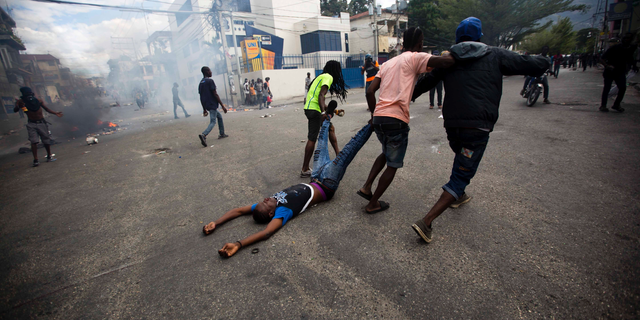 Demonstrators drag the body of a fellow protester toward police, as a form of protest after police shot into the crowd in which he died, during a demonstration demanding the resignation of Haitian President Jovenel Moise near the presidential palace in Port-au-Prince, Haiti, Tuesday, Feb. 12, 2019. Protesters are angry about skyrocketing inflation and the government's failure to prosecute embezzlement from a multi-billion Venezuelan program that sent discounted oil to Haiti. (AP Photo/Dieu Nalio Chery)