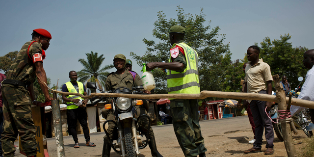 Two Congolese government soldiers have their feet and motorcycle tires sprayed with bleach as part of an Ebola containment programme on the road between Beni and Oicha, in Congo Friday, Feb. 1, 2019. The deadly Ebola outbreak in eastern Congo marked six months on Friday with officials noting a worrying number of confirmed cases linked to health centers.