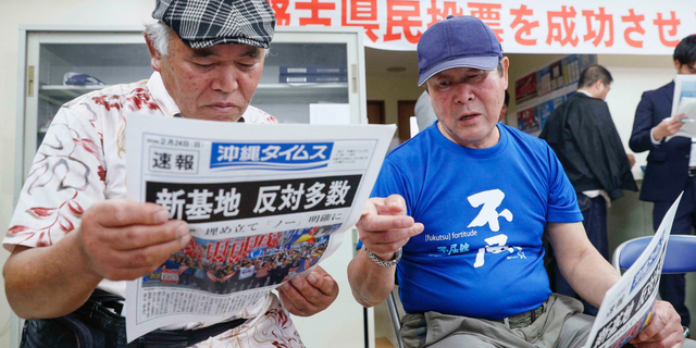 People take a look at a copy of a local newspaper reporting a referendum in Naha, Okinawa, Japan, Sunday, Feb. 24, 2019. The people of Okinawa voted Sunday on a plan for a U.S. military base relocation in a referendum that will send a message on how they feel about housing American troops in Japan, who many see as a burden on the group of tiny southwestern islands. The headline reads "New Base, Opposition majority."(Kyodo News via AP)