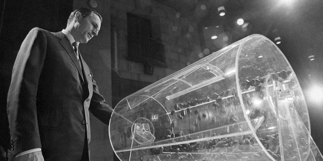 File-This Feb. 2, 1972, file photo shows Draft Director Curtis W. Tarr spinning one of the two Plexiglas drums in Washington as the fourth annual Selective Service lottery begins. The chairman of a panel considering changes to the U.S. military draft said Monday, Feb. 25, 2019, its recommendations to Congress won't be influenced by a federal judge's recent ruling that the current system is unconstitutional because it only applies to men. The military has not drafted anyone into service in more than 40 years, but American men must still register when they turn 18. Recent efforts to make registration also mandatory for women have set off intense debate in Washington. (AP Photo/Charles W. Harrity, File)