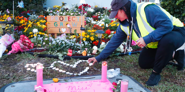 School crossing guard Wendy Behrend lights a candle at a memorial outside Marjory Stoneman Douglas High School during the one-year anniversary of the school shooting, Thursday, Feb. 14, 2019, in Parkland, Fla. A year ago on Thursday, 14 students and three staff members were killed when a gunman opened fire at the high school. (AP Photo/Wilfredo Lee)