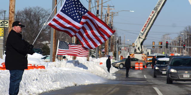 Timothy Nelson holds an American flag in front of Oak Creek Assembly of God Church in Oak Creek, Wis., showing support for the first responders on the day of Officer Matthew Rittner's funeral, Wednesday, Feb. 13, 2019. Rittner was killed in the line of duty Feb. 6. It is the sixth first-responder funeral that Nelson, who works at a senior care facility, has attended in the past 12 months. (Adam Rogan/The Journal Times via AP)