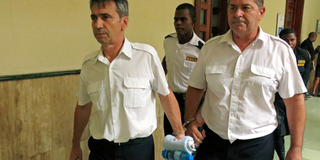 FILE - In this June 17, 2014 file photo, French pilots Bruno Odos, left, and Pascal Jean Fauret, who have been formally charged with drug trafficking, are escorted to a courtroom in Santo Domingo, Dominican Republic. Nine men go on trial in southern France for an alleged cocaine trafficking between the Caribbean and Europe, including two pilots who escaped the Dominican Republic to avoid 20-year prison sentences. (AP Photo/Ezequiel Abiu Lopez, File)
