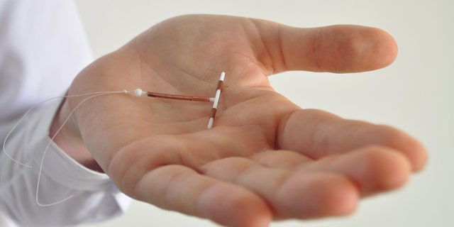 Holding a copper coil IUD birth control device in hand used for contraception - side view.