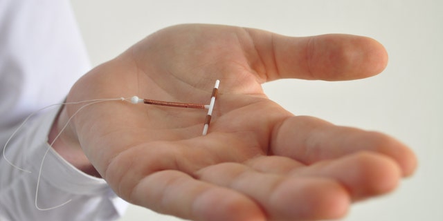 Holding an IUD birth control copper coil device in hand, used for contraception - side view