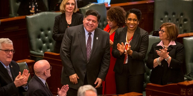 Illinois Gov. J.B. Pritzker, left, and Illinois Lt. Gov. Juliana Stratton, right, are acknowledged on the House floor at the Illinois State Capitol, Thursday, Feb. 14, 2019, in Springfield, Ill. Illinois legislators moved quickly to deliver one of Pritzker's top campaign promises, a gradual hike in the statewide minimum wage from $8.25 to $15 an hour, more than double the pay floor that most of its Midwestern neighbors require. (Justin L. Fowler/The State Journal-Register via AP)