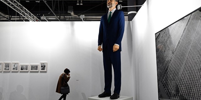 A woman talks on her mobile phone next to "Ninot", a giant sculpture depicting Spain's King Felipe VI by artists Santiago Sierra and Eugenio Merino, during preparations for the International Contemporary Art Fair (ARCO) in Madrid on February 26, 2019 on the eve of its inauguration.