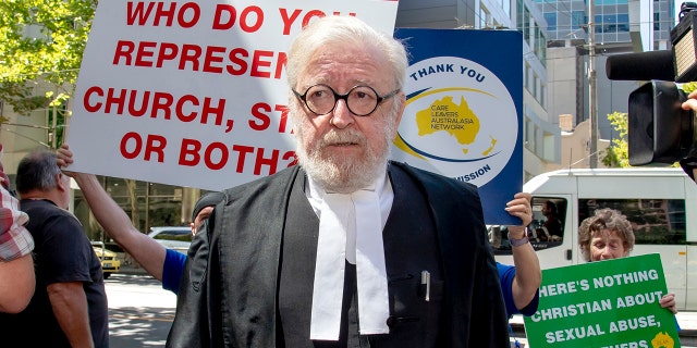 Cardinal George Pell's lawyer Robert Richter leaves the County Court as protesters hold placards in Melbourne, Australia, Wednesday, Feb. 27, 2019. The most senior Catholic cleric ever convicted of child sex abuse could face his first night in custody after a sentencing hearing Wednesday that will decide his punishment for molesting two choirboys in a Melbourne cathedral two decades ago. (AP Photo/Andy Brownbill)