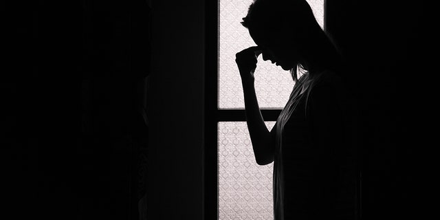 A depressed woman stands alone in a dark room. 
