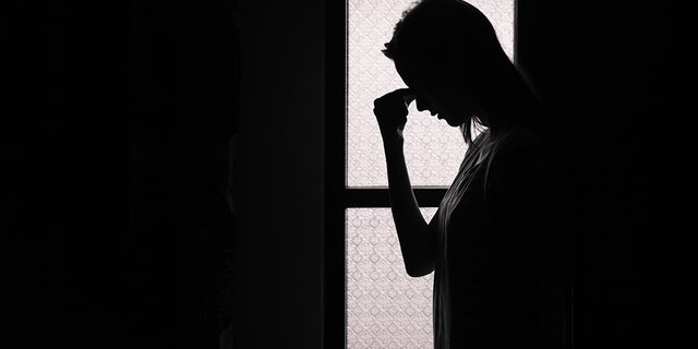 A depressed woman stands alone in a dark room. 