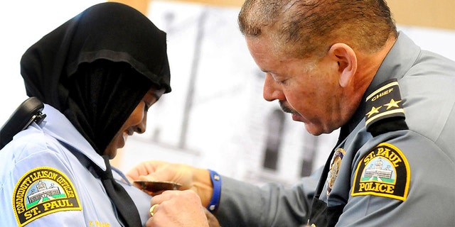 In this March 1, 2014 file photo, St. Paul, Minn. Community Officer Kadra Mohamed, left, smiles as she receives her badge from St. Paul, Minn. Police Chief Thomas Smith, during a ceremony for her and the East African Junior Police Academy at the Western District Police Station in St. Paul, Minn. (Sherri LaRose-Chiglo/Pioneer Press via AP)