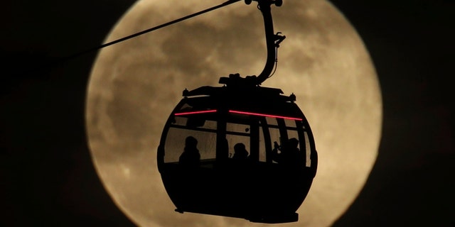 An Emirates Air Line cable cars is silhouetted against the backdrop of the 'supermoon' in Greenwich, London, Tuesday, Feb. 19, 2019.