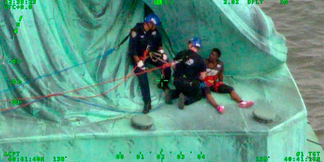 In this July 4, 2018, frame from video provided by the New York City Police Department, members of the NYPD Emergency Service Unit work to safely remove Therese Okoumou, a protester who climbed onto the Statue of Liberty and was charged with misdemeanor trespassing and disorderly conduct. (NYPD via AP)