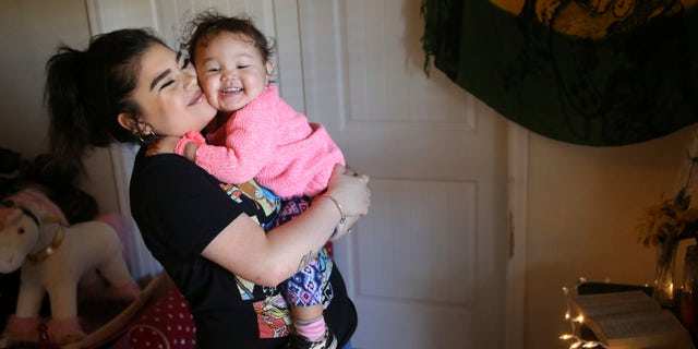 Seanna Leilani Chavez, left, holds Athena Chavez, 2, the sister and daughter of Aaron Francisco Chavez respectively, as the two stand next to a shrine for Aaron at the family home.