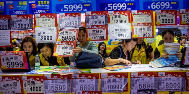 In this March 3, 2018, photo, people check on travel packages offered by travel agencies during the Guangzhou International Travel Fair in Guangzhou in south China's Guangdong province. Travelers in China were blocked from buying plane tickets 17.5 million times last year as a penalty for failing to pay fines or other offenses. The Chinese government reported this week on penalties imposed under a controversial "social credit" system the ruling Communist Party says will improve public behavior. (Chinatopix via AP)