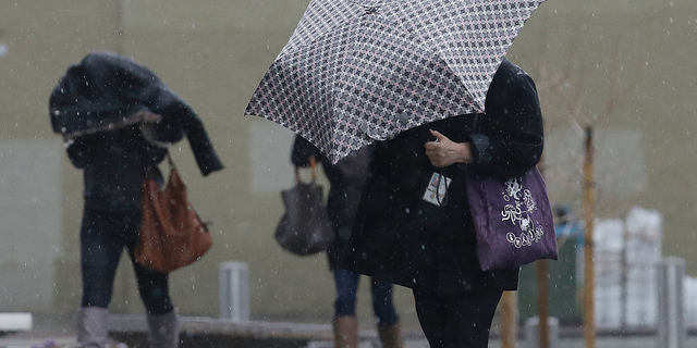 Women walk in the rain toward a federal court building in San Francisco, Monday, Feb. 25, 2019. A fierce winter storm packing winds in excess of 100 mph (160 kph) and predicted to bring as much as 8 feet (2.4 meters) of snow to the Sierra Nevada barreled into the West Coast on Monday, toppling trucks, triggering power outages and temporarily closing the major highway near Reno. (AP Photo/Jeff Chiu)