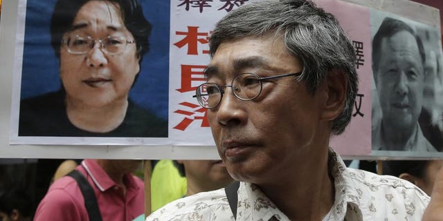 In this June 18, 2016, file photo, freed Hong Kong bookseller Lam Wing-kee stands next to a placard with picture of missing bookseller Gui Minhai, in front of his book store in Hong Kong as the protesters are marching to the Chinese central government's liaison office. Sweden has condemned China's "brutal" detention of a Swedish citizen who sold politically sensitive books and whose seizure while he traveled with diplomats stunned Western governments.