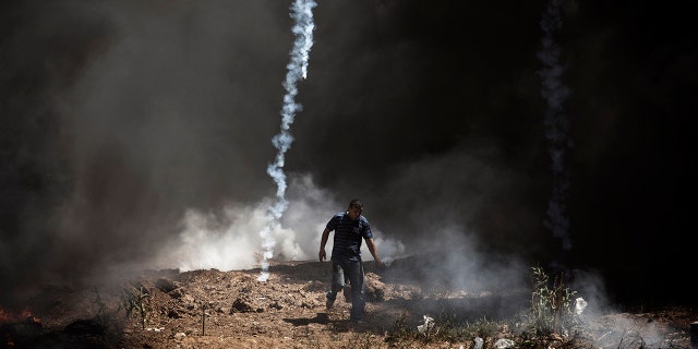 A tear gas canister falls near a Palestinian at the border fence with Israel as mass demonstrations continue on May 14, 2018 in Gaza City, Gaza.