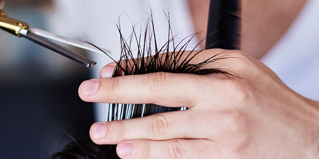 Close-up photo of barber’s hands with scissors cutting hair