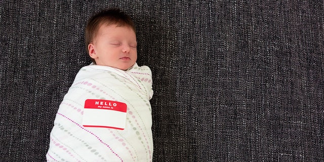 Sleeping swaddled infant with a "Hello my name is" sticker.