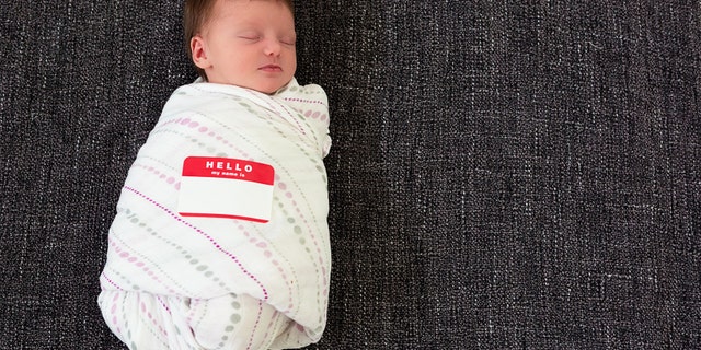 Sleeping swaddled infant with a "Hello my name is" sticker.