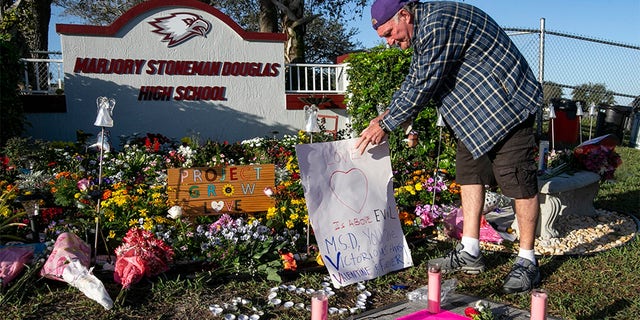 Jack Jozefs places a sign at a memorial outside Marjory Stoneman Douglas High School, Thursday, on the one-year anniversary of the deadly shooting at the school that killed 17 people, in Parkland, Florida.