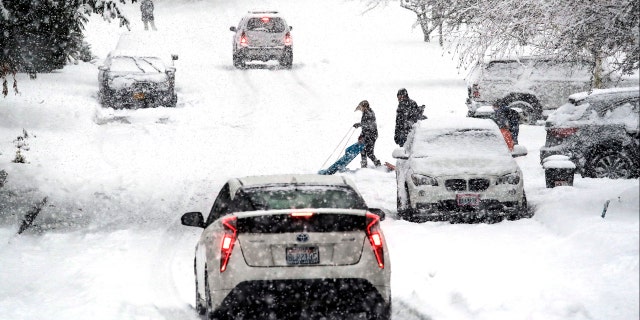 A sledder moves aside as traffic heads downhill in heavy snow falling Monday, Feb. 11, 2019, in Seattle.
