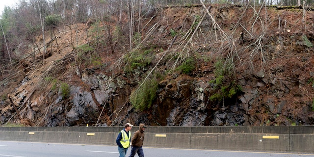 Workers walk past the scene of a mudslide on I-40 heading east to Clyde, northeast, near the border between Tennessee and North Carolina, on Saturday, February 23 2019.