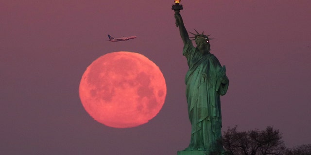 The 'super snow moon' sets behind the Statue of Liberty in New York City as the sun rises on Feb. 19, 2019.