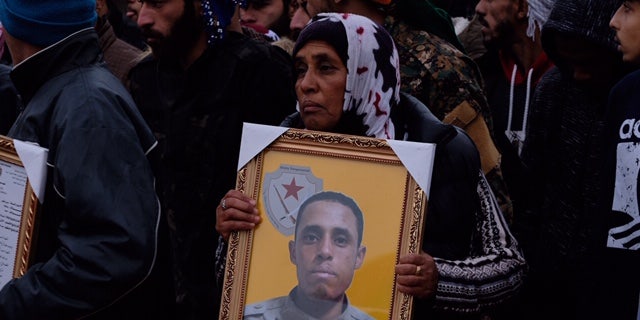 A lamentation mom binds a mural of her son who was killed fighting ISIS in Deir-ez-Zor in Jan 2019.
