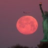 The Super Snow Moon sets behind the Statue of Liberty as the sun rises in New York City, Feb. 19, 2019. 