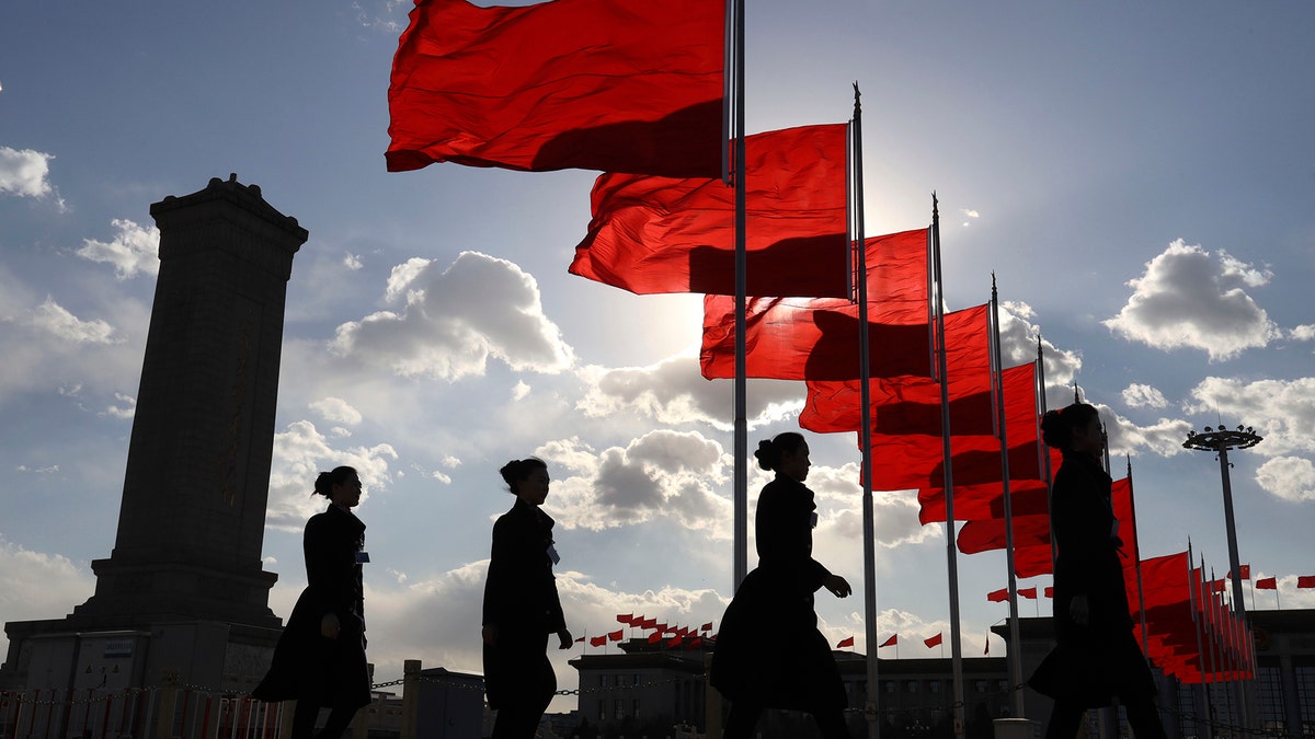 Bus ushers walk past red flags on Tiananmen Square during a plenary session of the Chinese People's Political Consultative Conference (CPPCC) at the Great Hall of the People in Beijing Monday, March 11, 2019. (AP Photo/Ng Han Guan)