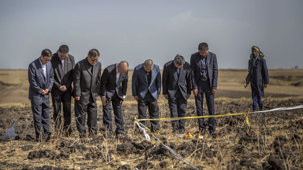 Officials from the Aviation Industry Corporation of China (AVIC) pray next to an offering of fruit, bread rolls, and a plastic container of Ethiopian Injera, a fermented sourdough flatbread, placed next to incense sticks, at the scene where the Ethiopian Airlines Boeing 737 Max 8 crashed shortly after takeoff on Sunday killing all 157 on board, near Bishoftu, or Debre Zeit, south of Addis Ababa, in Ethiopia.