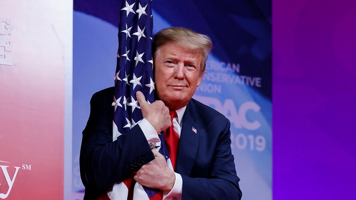 President Donald Trump hugs the American flag as he arrives to speak at Conservative Political Action Conference, CPAC 2019, in Oxon Hill, Md., Saturday, March 2, 2019. (Associated Press)