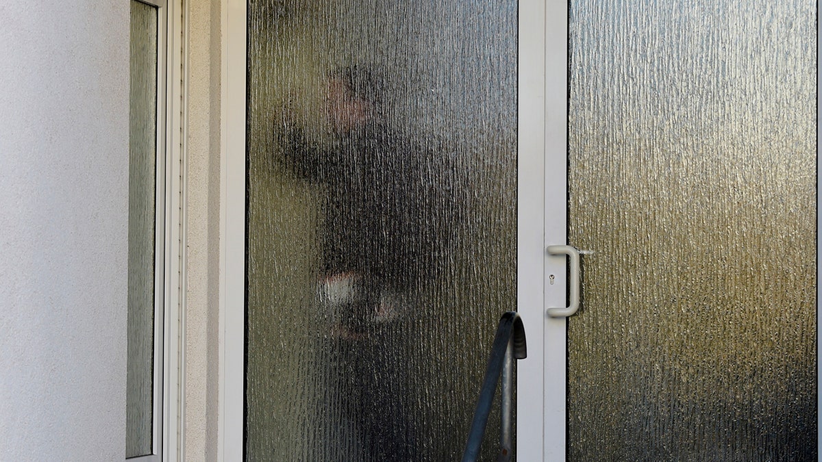 A customs officer walks behind a glass door of a house with a doctor's office during a doping raid in Erfurt, Germany, Wednesday, Feb. 27, 2019. Several people were arrested in doping raids in Austria and Germany during the Nordic skiing world championships.