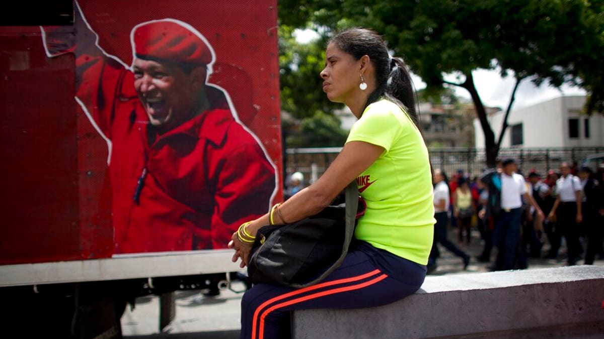 A supporter of Venezuela's President Nicolas Maduro sits next to an image depicting the late president Hugo Chavez during an "anti-intervention" march coinciding with the anniversary of the deadly 1989 social uprising against neoliberal measures known as the Caracazo, in Caracas, Venezuela, Wednesday, Feb. 27, 2019. (AP Photo/Ariana Cubillos)