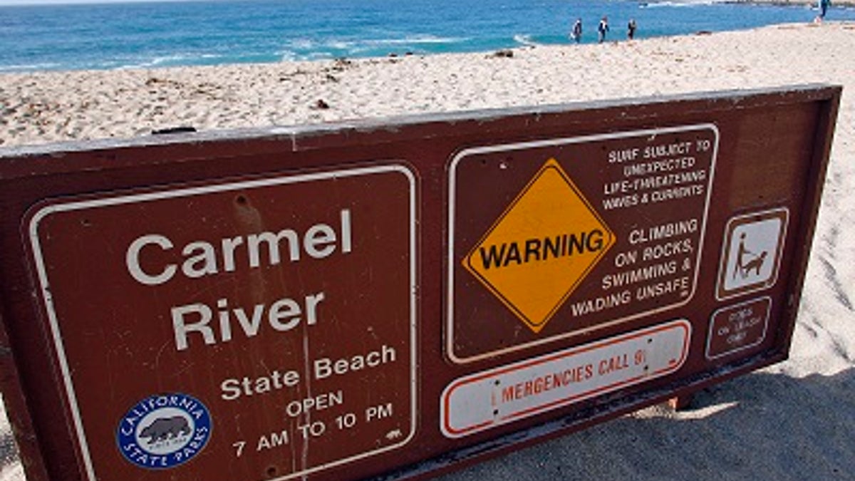 A warning sign shows the dangerous conditions near the Monastery Beach area of Carmel River State Beach in Carmel, Calif.