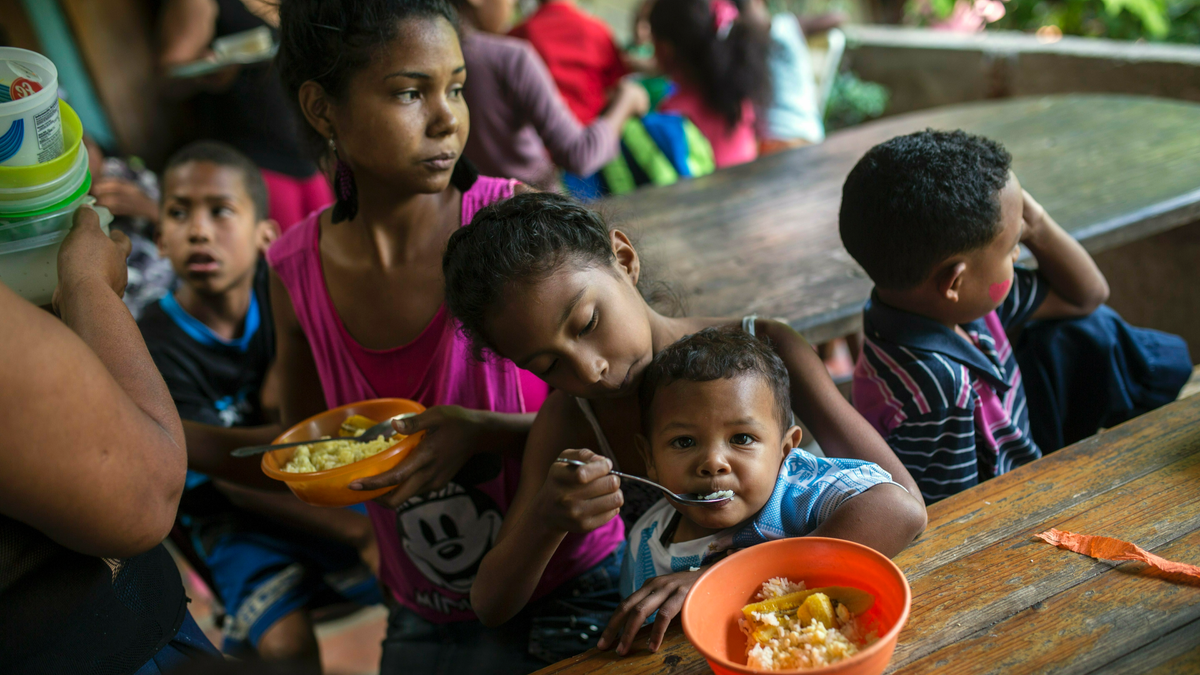 Eight-year-old Franyelis feeds her baby brother Joneiber as their mother Francibel Contreras holds a bowl of scrambled eggs and rice, at a soup kitchen in the Petare slum, Caracas, Venezuela. Contreras brings her three malnourished children to the soup kitchen in the dangerous hillside slum where they scoop in spoonfuls of food in what could be their only meal of the day. (AP Photo/Rodrigo Abd)