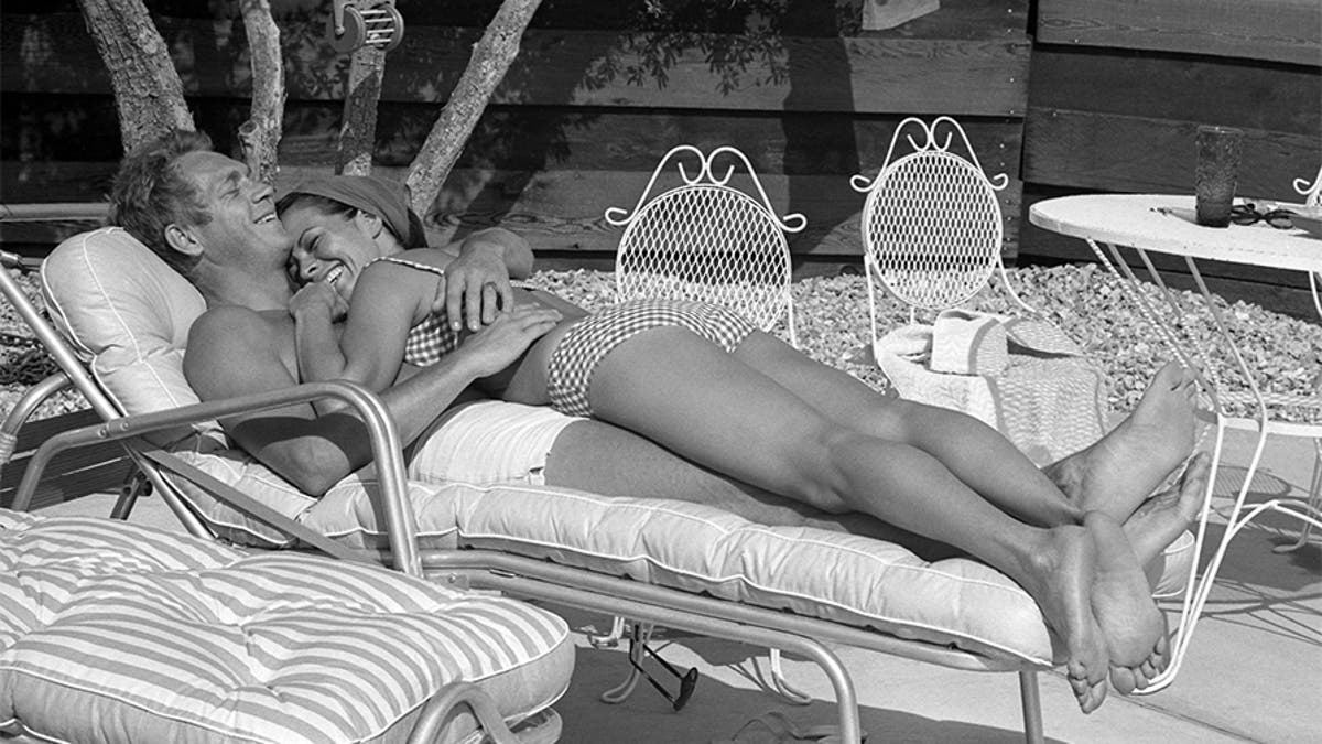 Philippine-born actress Neile Adams lies on top of her husband, American actor Steve McQueen (1930-1980), on a deckchair next to the pool at their home, Palm Springs, Calif., May 1963.