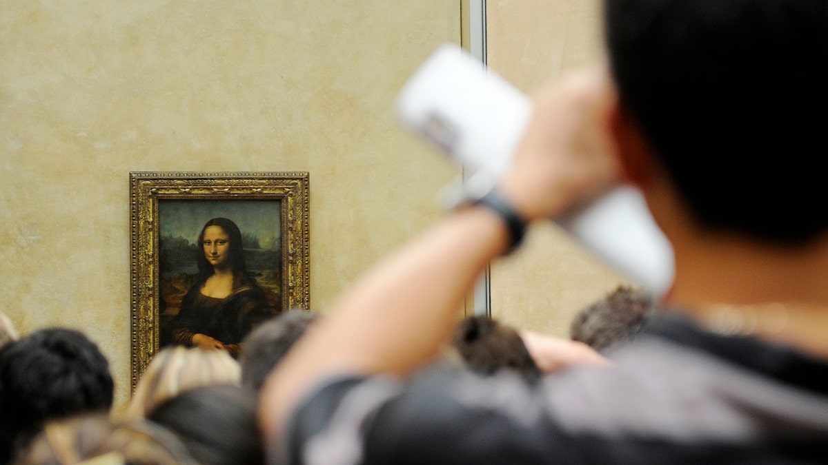 A tourist takes souvenir photos of Italian painter Leonardo da Vinci's famed portrait Mona Lisa at the Louvre Museum in Paris, Aug. 12, 2009.