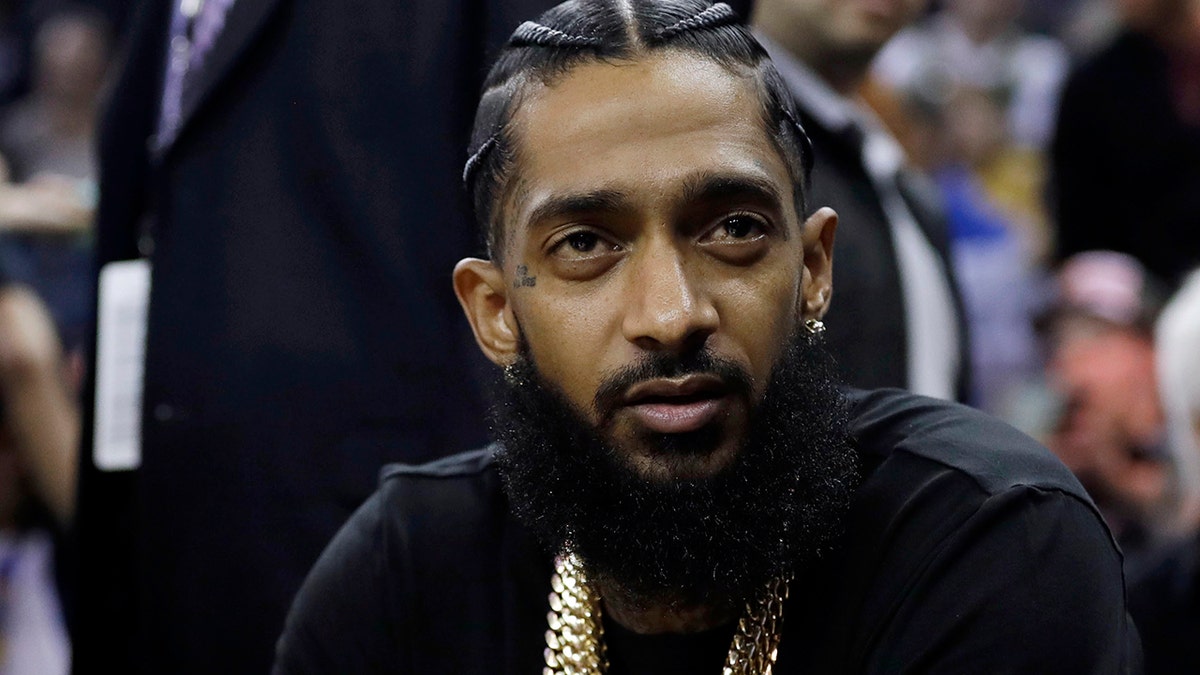 FILE - In this March 29, 2018, file photo, rapper Nipsey Hussle watches an NBA basketball game between the Golden State Warriors and the Milwaukee Bucks in Oakland, Calif. Grammy-nominated and widely respected West Coast rapper Nipsey Hussle has been shot and killed outside his Los Angeles clothing store, Los Angeles Mayor Eric Garcetti said Sunday, March 31, 2019. He was 33. (AP Photo/Marcio Jose Sanchez, File)