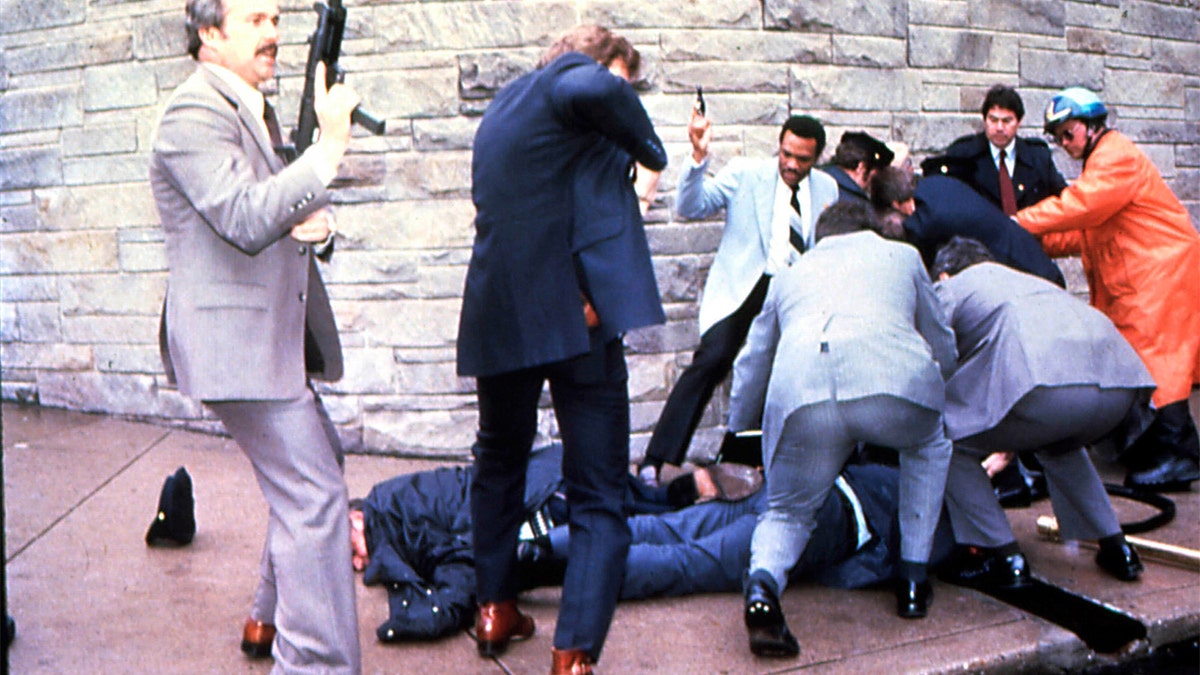 FILE - James Brady and a police officer are seen lying on the ground after being shot while the suspect John Hinckley Jr. is apprehended, at right, moments after the attempted assassination of President Ronald Reagan, Washington, DC, March 30, 1981. (Photo by Dirck Halstead/Getty Images)