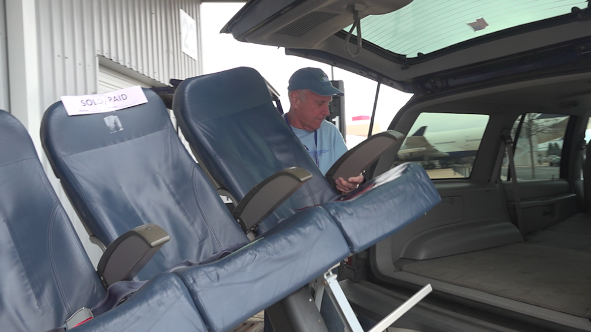 Volunteers load a set of airplane seats into a shopper's trunk at the Delta Surplus Sale.