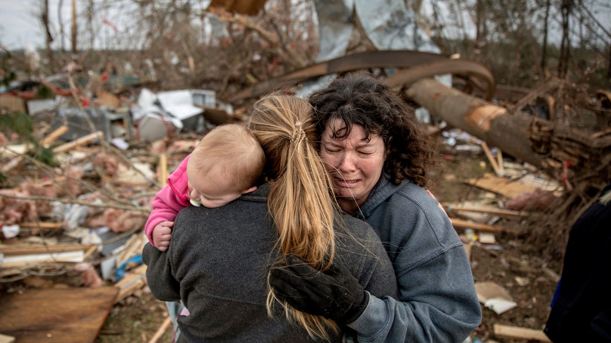 Carol Dean, right, cries while embraced by Megan Anderson and her 18-month-old daughter Madilyn, as Dean sifts through the debris of the home she shared with her husband, David Wayne Dean, who died when a tornado destroyed the house in Beauregard, Ala., Monday, March 4, 2019.