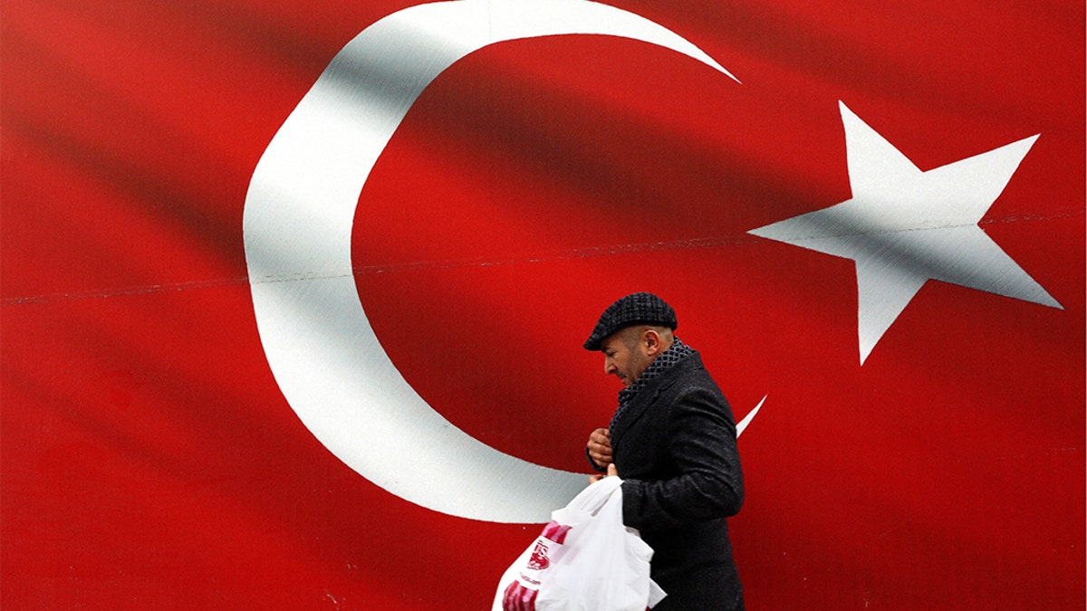 A man walking by a giant Turkish flag in Ankara, Turkey, on Sunday. Turkish citizens have begun casting votes in municipal elections for mayors, local assembly representatives and neighborhood or village administrators. (AP Photo/Ali Unal)