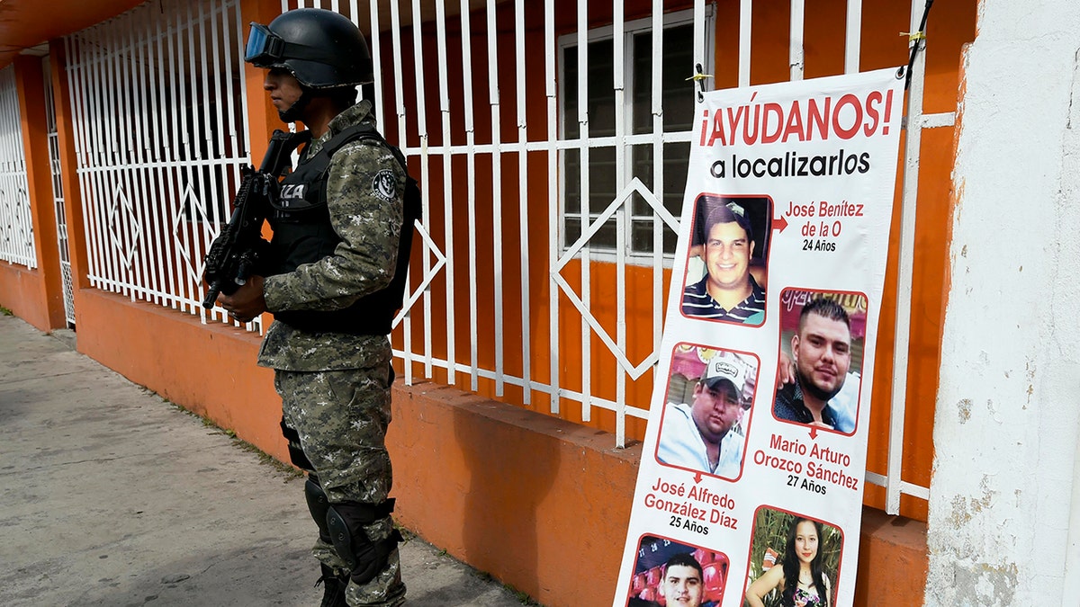 A Civil Forces police officer stands next to a banner with pictures of five youngsters who went missing January 11, 2016, in Tierra Blanca community, Veracruz State, Mexico.