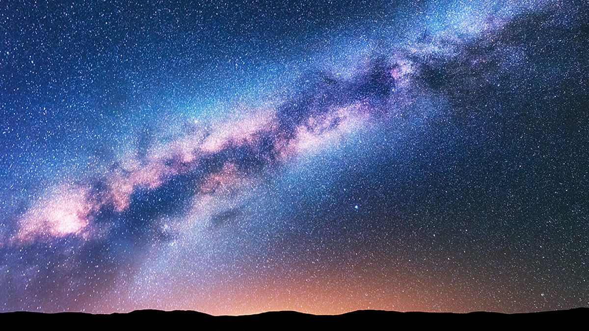 Milky Way. Fantastic night landscape with purple milky way, sky full of stars, yellow light and hills. Shiny stars. Beautiful scene with universe. Space background with starry sky. Astrophotography.
