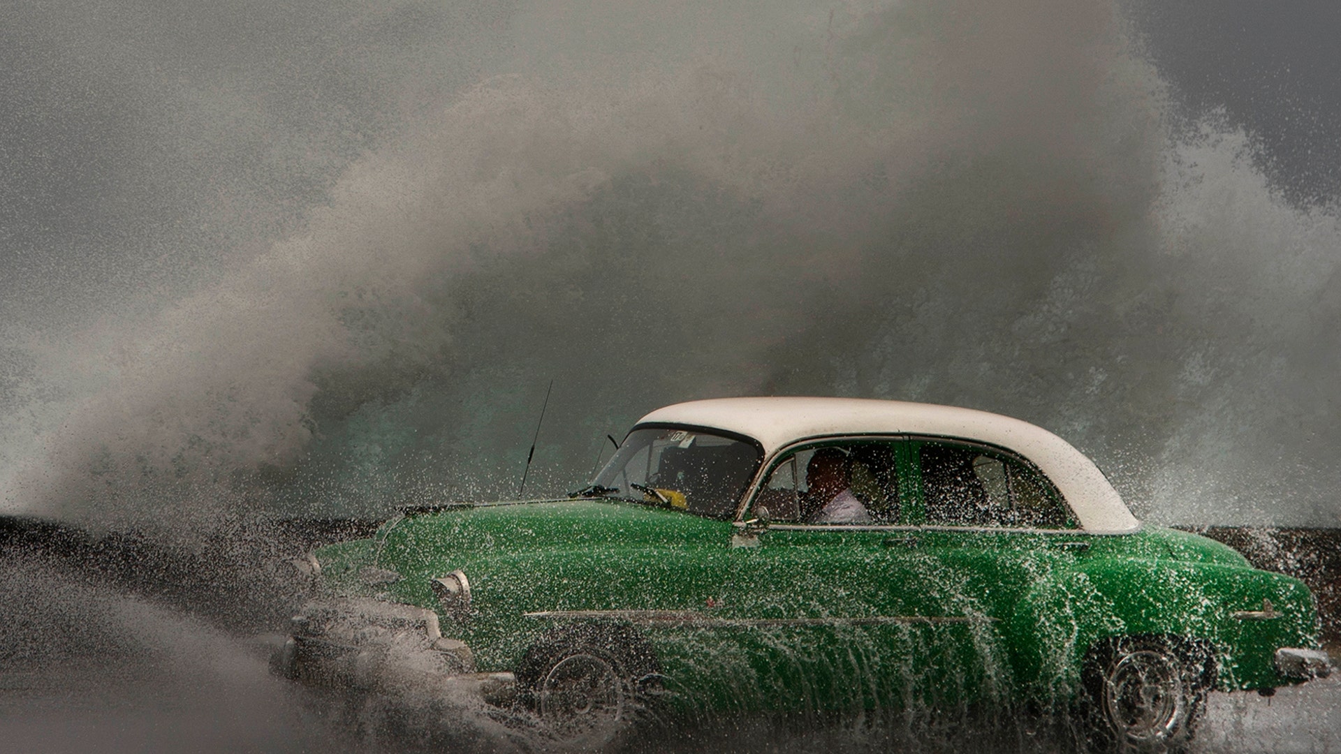 Waves crash against the Malecon sea wall as a taxi drives past in a classic American car in Havana, Cuba, March 19, 2019.