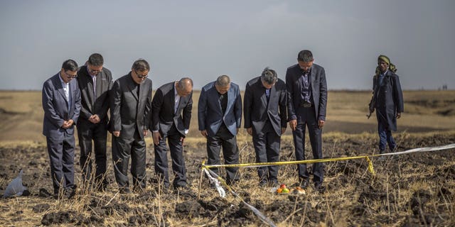 Officials from the Aviation Industry Corporation of China (AVIC) pray next to an offering of fruit, bread rolls, and a plastic container of Ethiopian Injera, a fermented sourdough flatbread, placed next to incense sticks, at the scene where the Ethiopian Airlines Boeing 737 Max 8 crashed shortly after takeoff on Sunday killing all 157 on board, near Bishoftu, or Debre Zeit, south of Addis Ababa, in Ethiopia.
